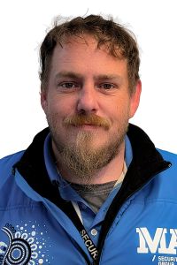 A security guard working at 15 William Street wearing a blue polo shirt with a black collar and a lanyard