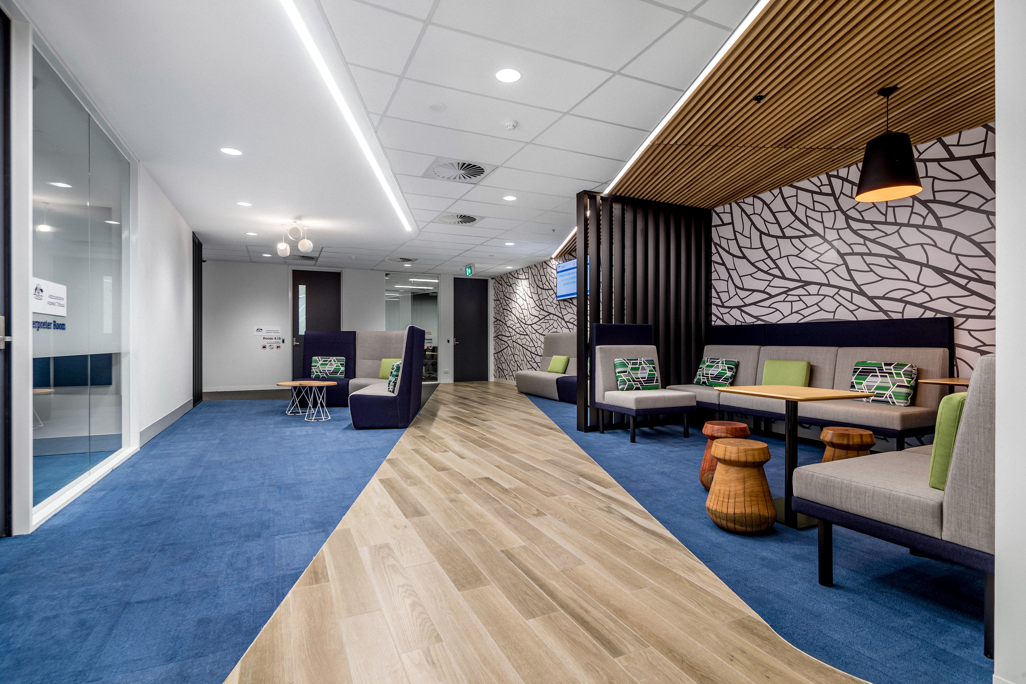 Waiting area in Melbourne registry. There are meeting rooms with glass walls and doors to the left with a plush seating area to the right. The room is brightly lit and colourful with blue carpet and green couch cushions.